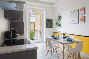 A modern kitchen with a coffee machine, a dining area with a table set for two, and a balcony with a view.