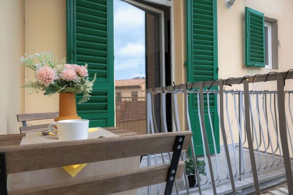 A balcony with a wooden bench, a white mug, and a vase with flowers.