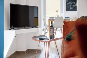 A living room with a TV, a small table with a wine bottle and glasses, a sofa, and a view of the outside.