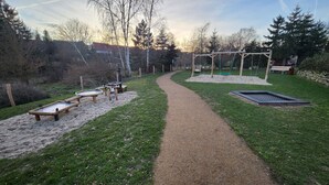 Un sendero de grava que atraviesa un área cubierta de césped con juegos infantiles al aire libre y una estructura de madera.