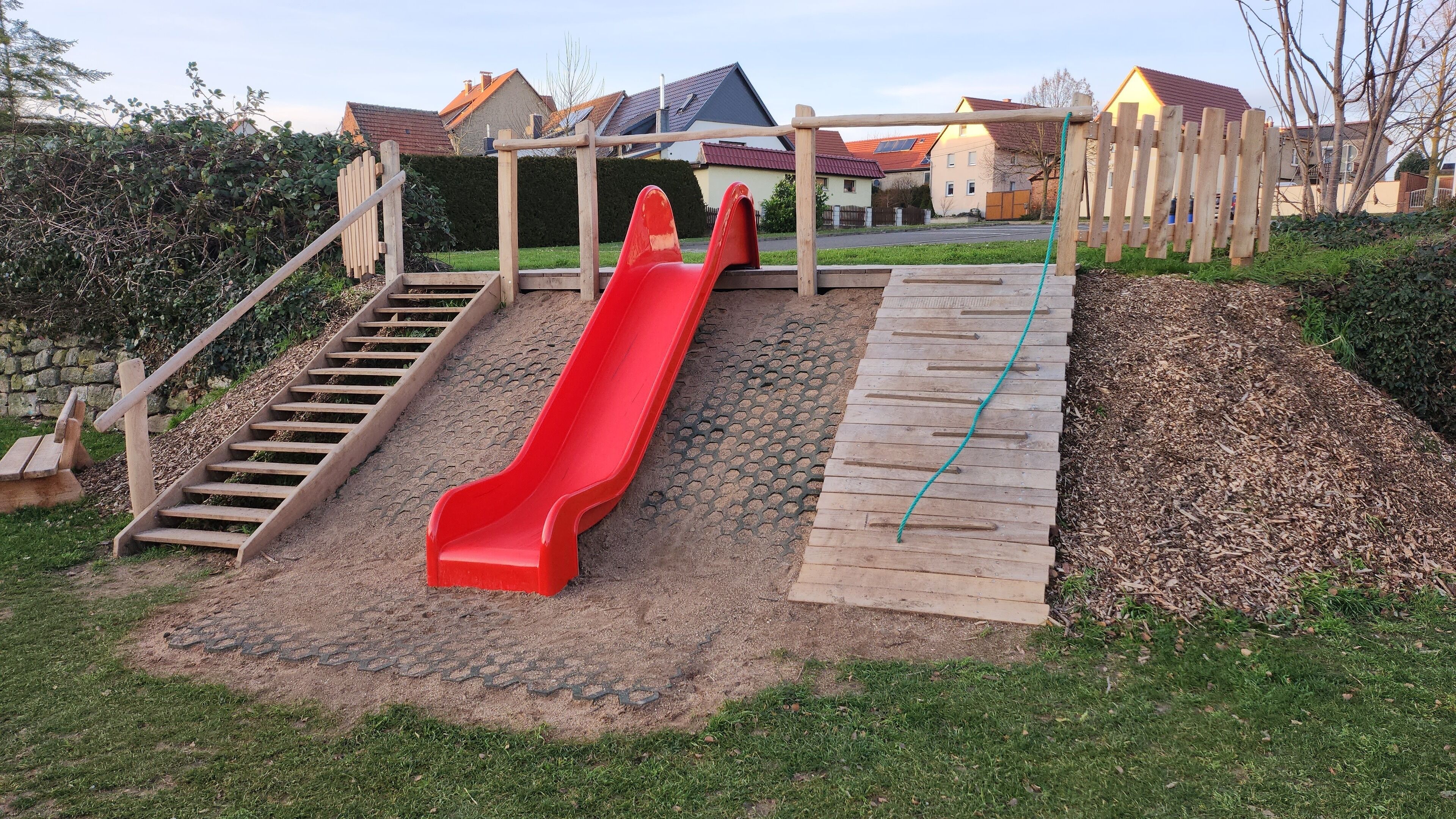 A playground with a red slide, wooden stairs, and a wooden climbing structure.