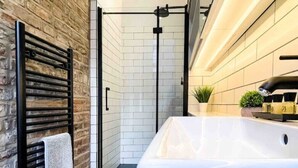 A modern bathroom with a large bathtub, a towel rack with a towel, a glass shower enclosure, and a small plant on the countertop.