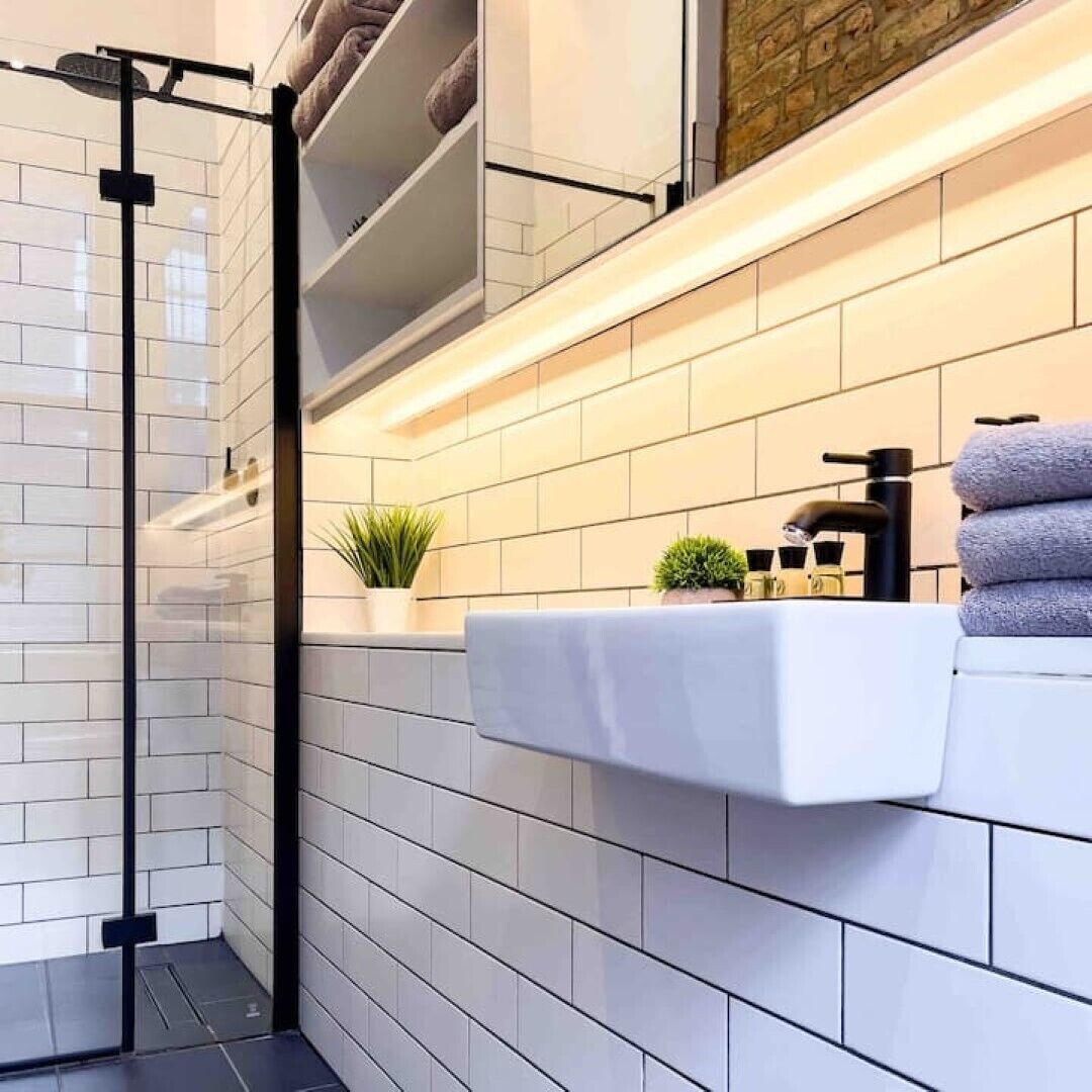 Un baño moderno con azulejos blancos tipo metro, cabina de ducha de vidrio, encimera blanca con una toalla y una pequeña planta en maceta.