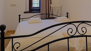 Un dormitorio con cama, una ventana con cortinas, una araña y una mesita.