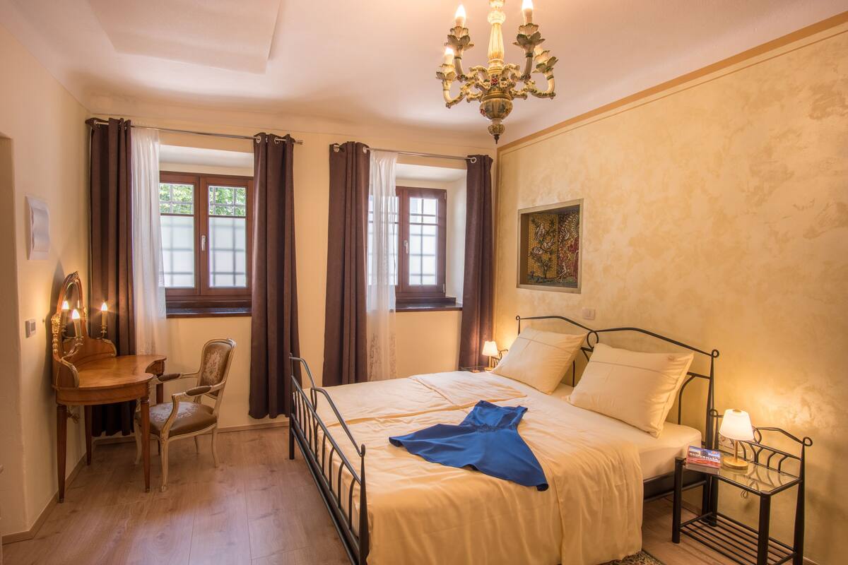 Un dormitorio con cama, escritorio con silla, candelabro y un cuadro en la pared.
