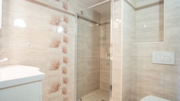 Un baño moderno con ducha de vidrio, lavamanos blanco y retrete.