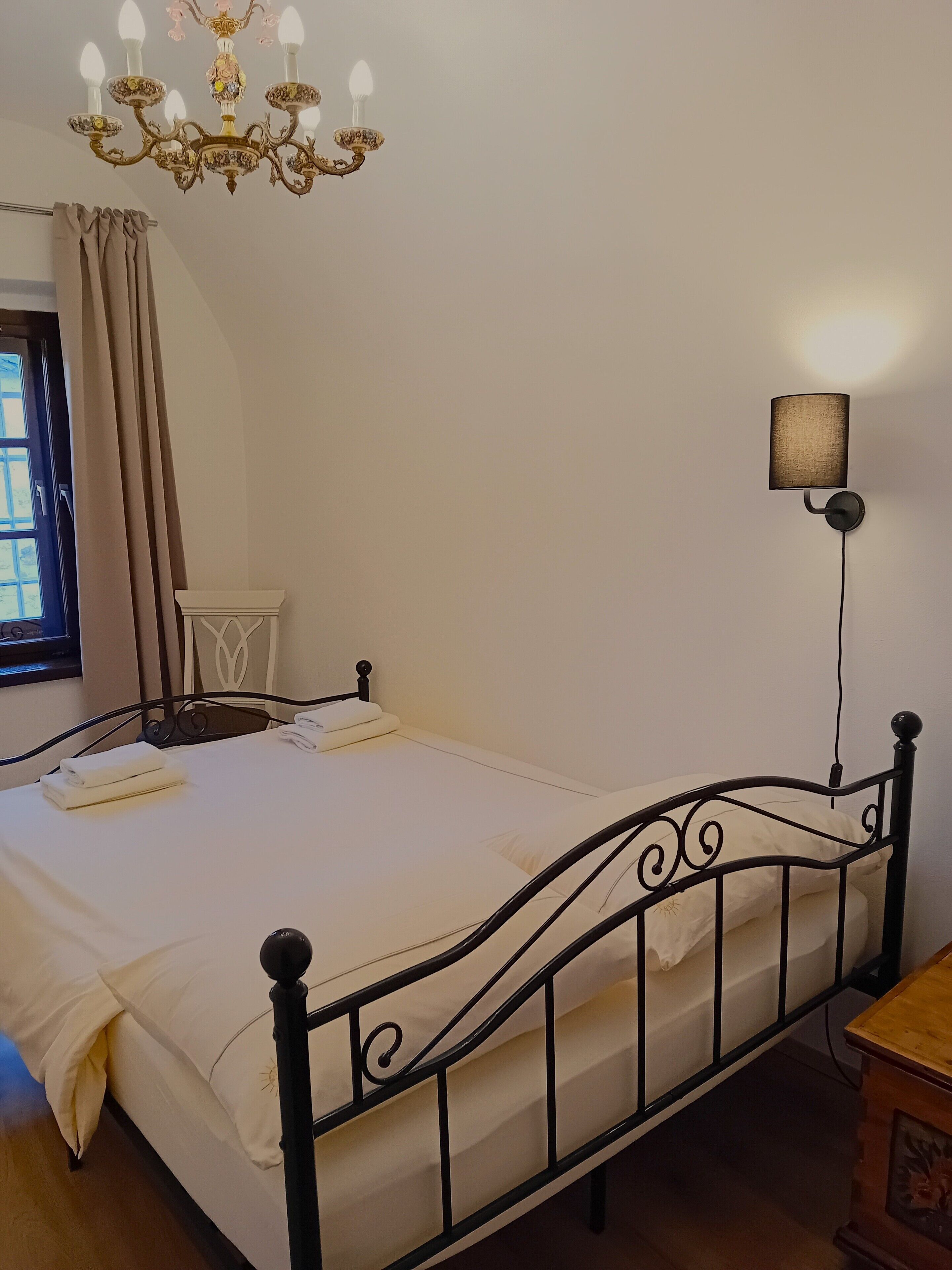 A neatly made bed with white linens, a black metal headboard, and a wall-mounted lamp.