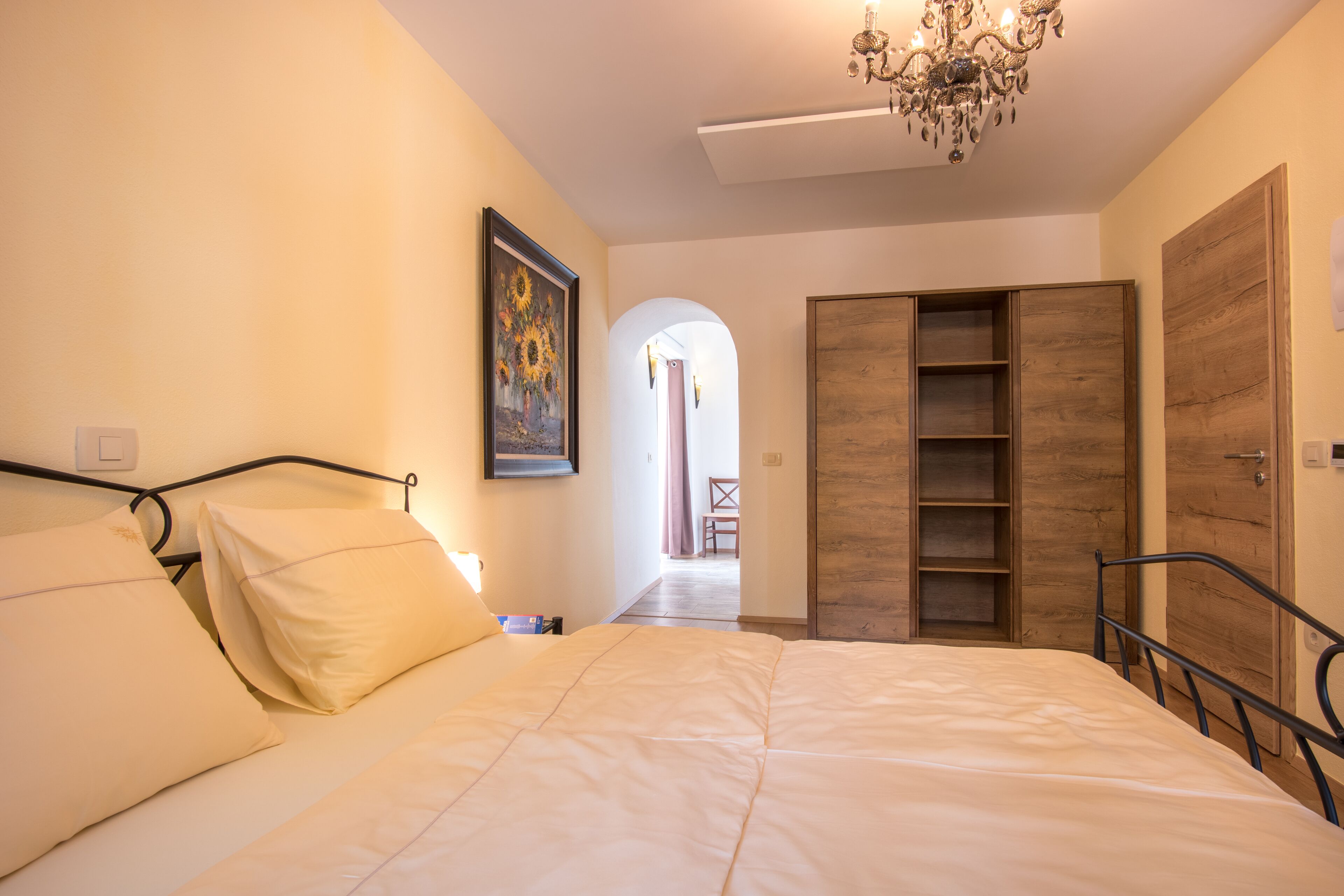 A bedroom with a large bed, a wooden wardrobe, and a painting on the wall.