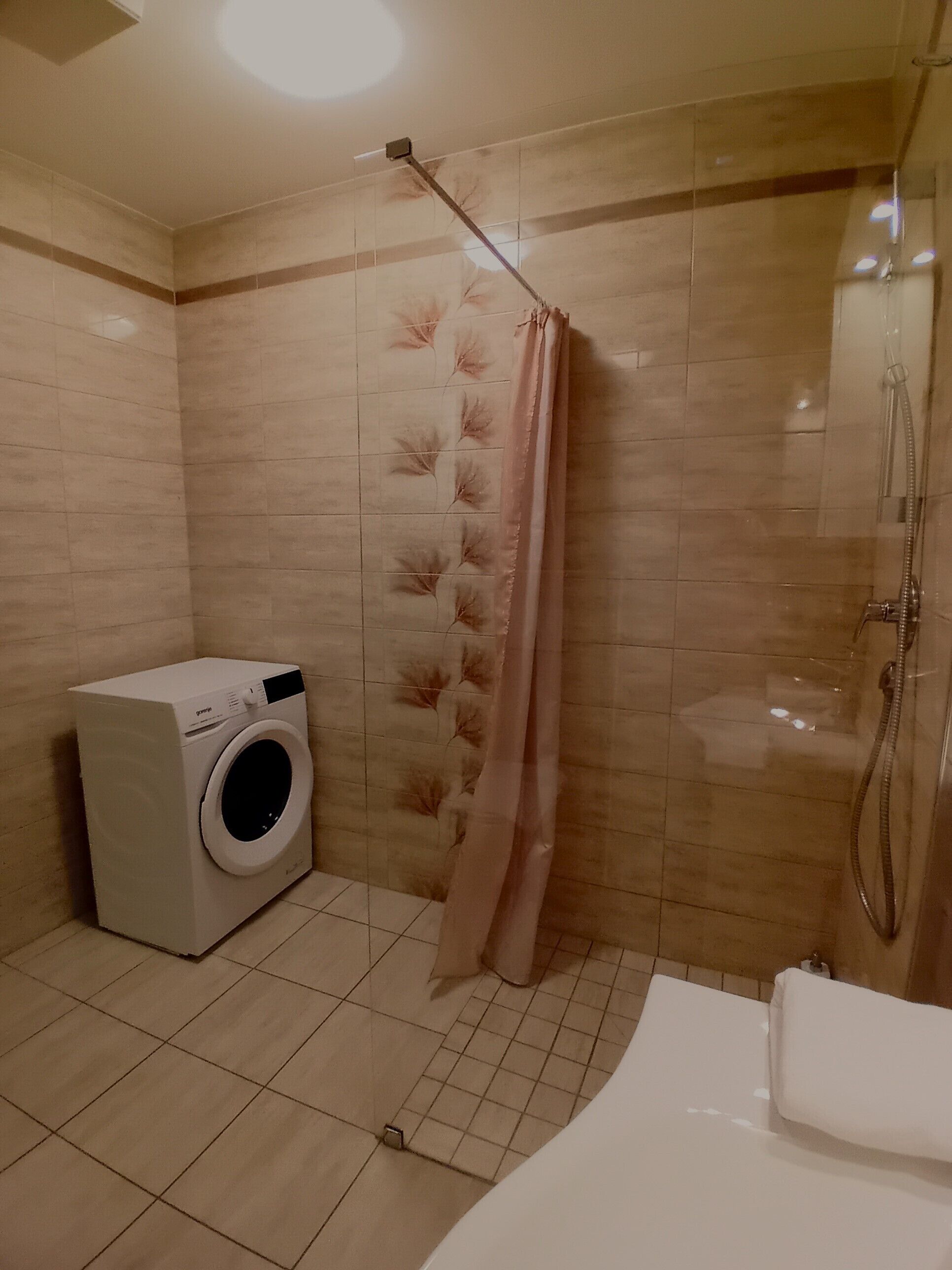 Een kleine badkamer met een wasmachine, een douche met gordijn en een bad.