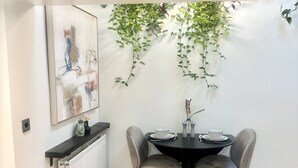 A dining area with a black table and grey upholstered chairs, a radiator below, and a wall-mounted plant. - Cosy and Stylish Studio Apartment
 (Trowbridge)