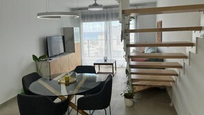 Un salon moderne comprenant un coin repas, un téléviseur posé sur un meuble et un escalier avec des marches en bois.