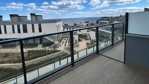 Un balcon offrant une vue sur une zone côtière, avec des bâtiments modernes et un ciel dégagé.