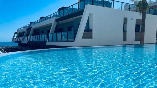 Un hôtel moderne doté d’une piscine, d’un palmier et offrant une vue sur l’océan.