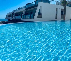 Een modern hotel met een zwembad, een palmboom en uitzicht op de oceaan.