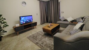 A modern living room with a flat-screen TV, a sofa, a coffee table, and a plant. - City Center: Modern 2BR Flat-56 (Cairo Governorate)