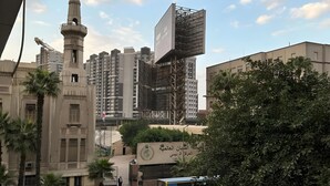 A cityscape with a prominent mosque, high-rise buildings, and a billboard. - City Center: Modern 2BR Flat-56 (Cairo Governorate)