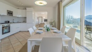 A modern kitchen with white cabinets, a dining area with a table set for four, and a large sliding glass door leading to an outdoor patio. - Varenna O Sole Mio in Perledo (Perledo)