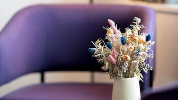 Una silla morada, una mesita con un jarrón de flores secas y una lámpara de pie al fondo.