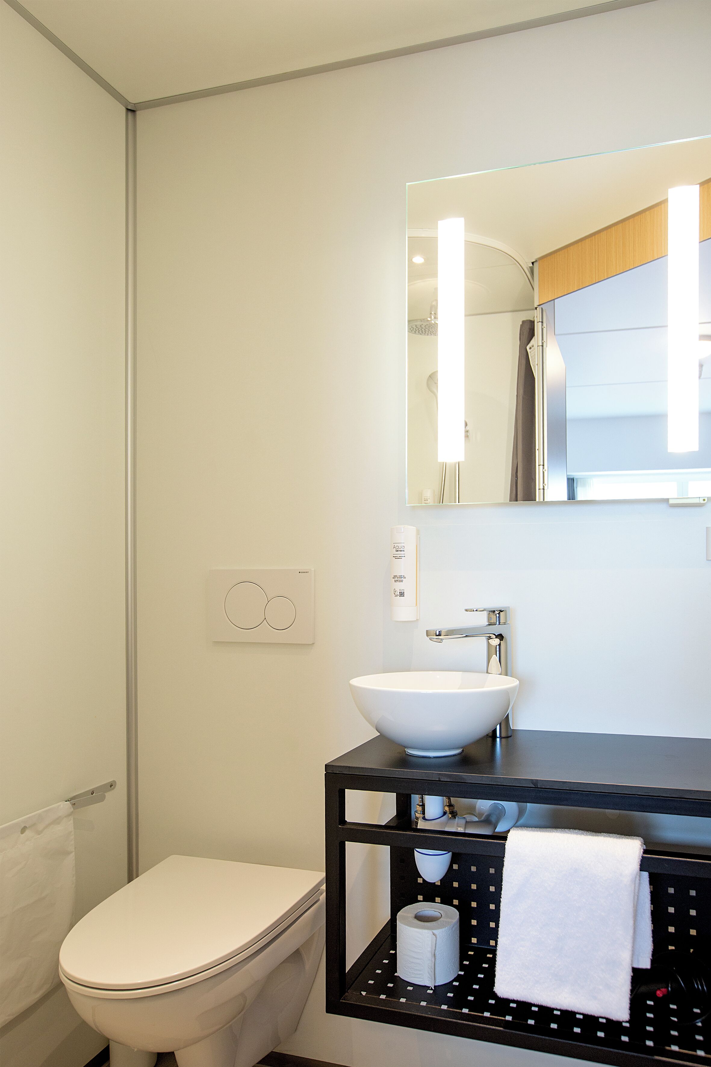 A modern bathroom with a white toilet, a black sink with a mirror above, and a towel rack with a white towel.