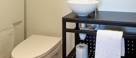 A modern bathroom with a white toilet, a black sink with a mirror above, and a towel rack with a white towel.