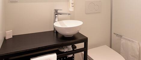 Un bagno moderno con lavandino bianco, mobile contenitore nero e vaso igienico bianco.
