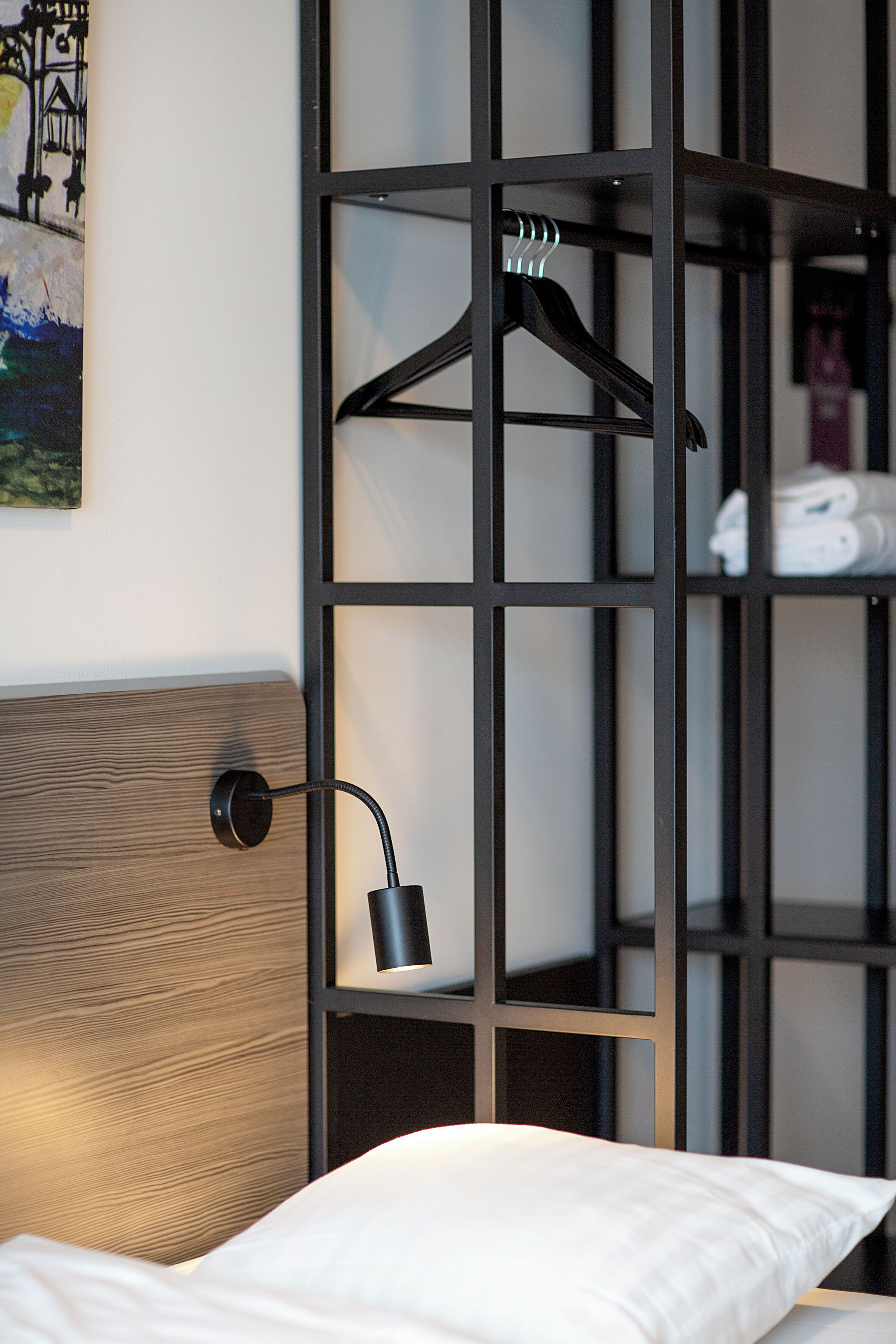 Una habitación de hotel moderna con cabecera de madera, armario de metal negro y lámpara colgante.