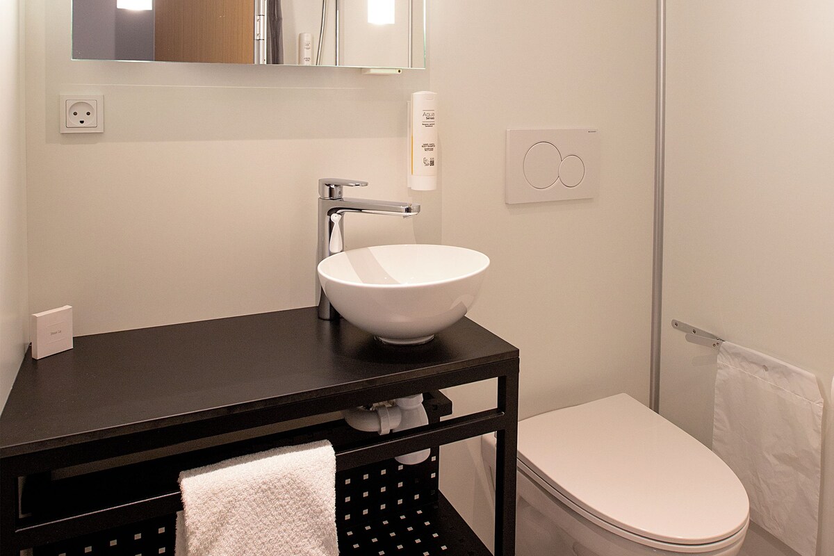Ein modernes Badezimmer mit einem weißen Waschbecken, einer schwarzen Kommode und einer weißen Toilette.