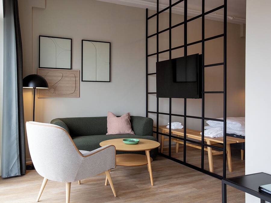 Una sala de estar moderna con un sofá verde, un sillón gris, una mesa de centro redonda de madera y un televisor negro montado en una pared divisoria negra.