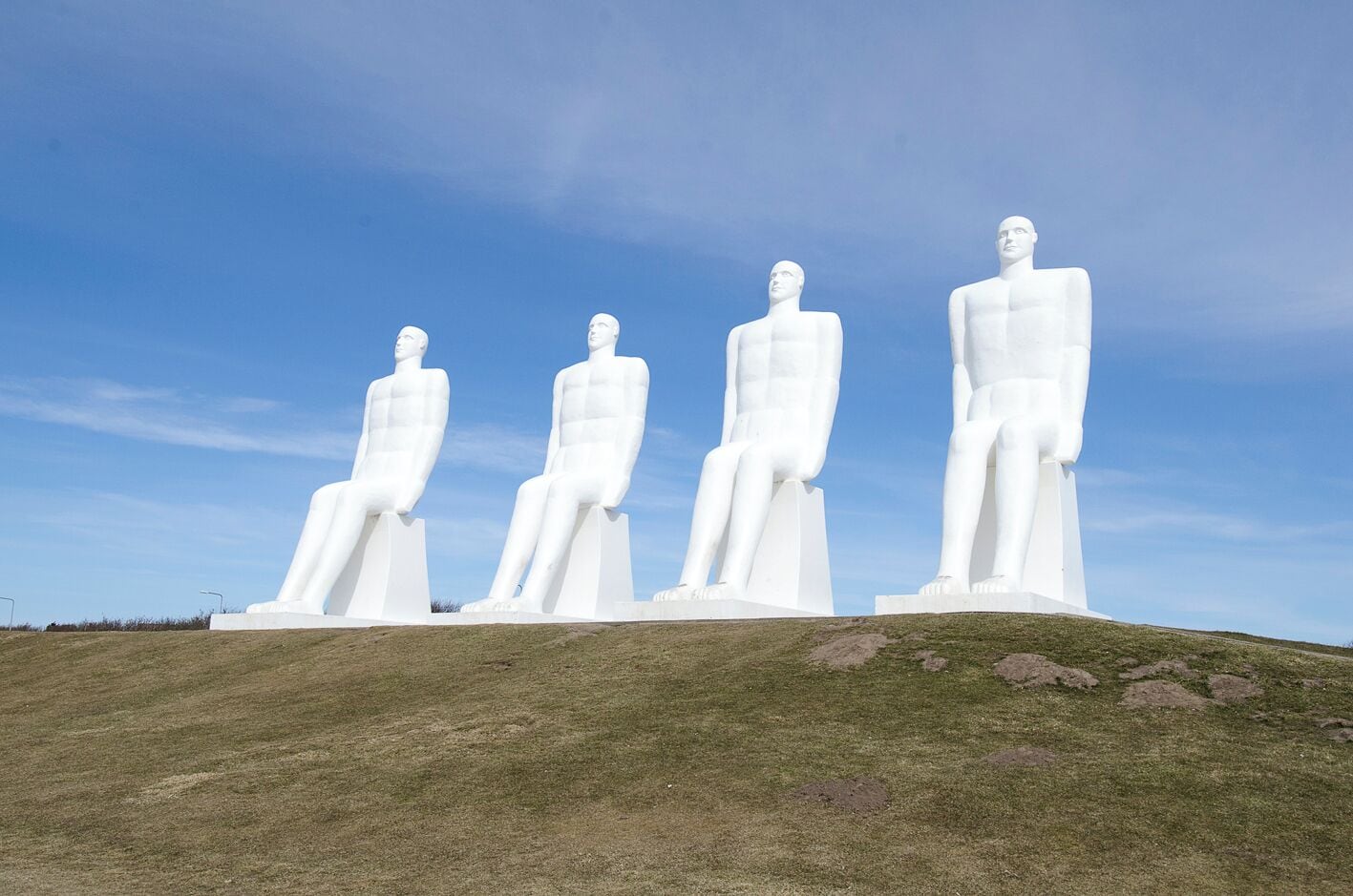 Four large white statues on a grassy hill under a clear sky.