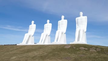 Four large white statues on a grassy hill under a clear sky.