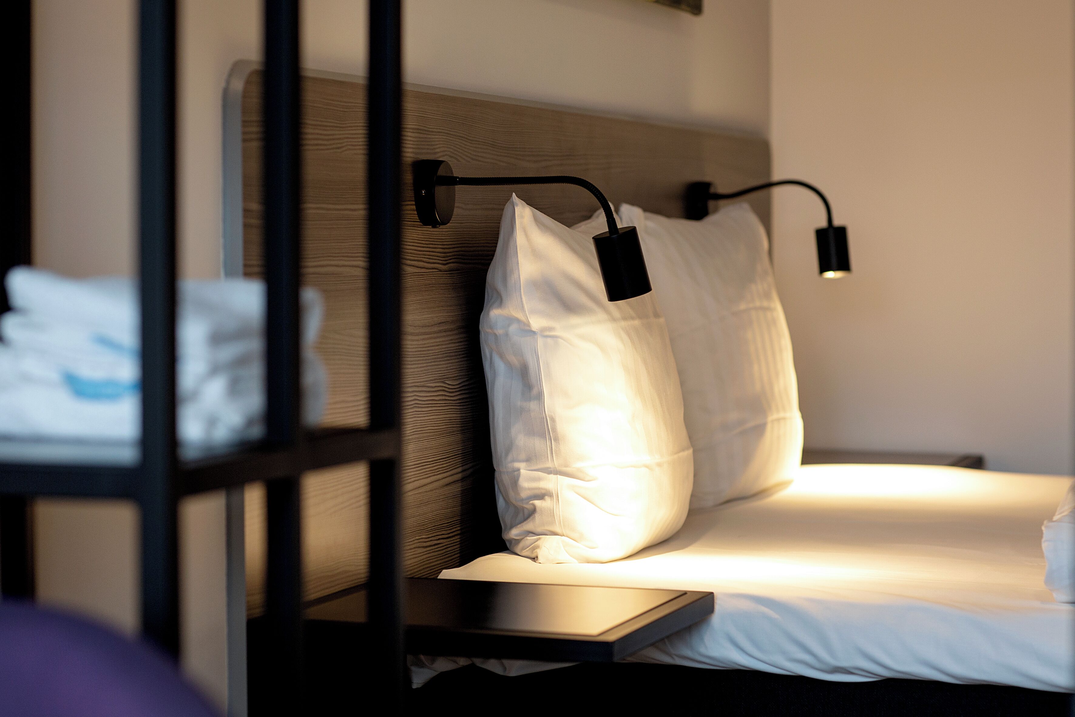 Un letto rifatto con lenzuola bianche e due cuscini, un comodino con una lampada e una testiera in legno.