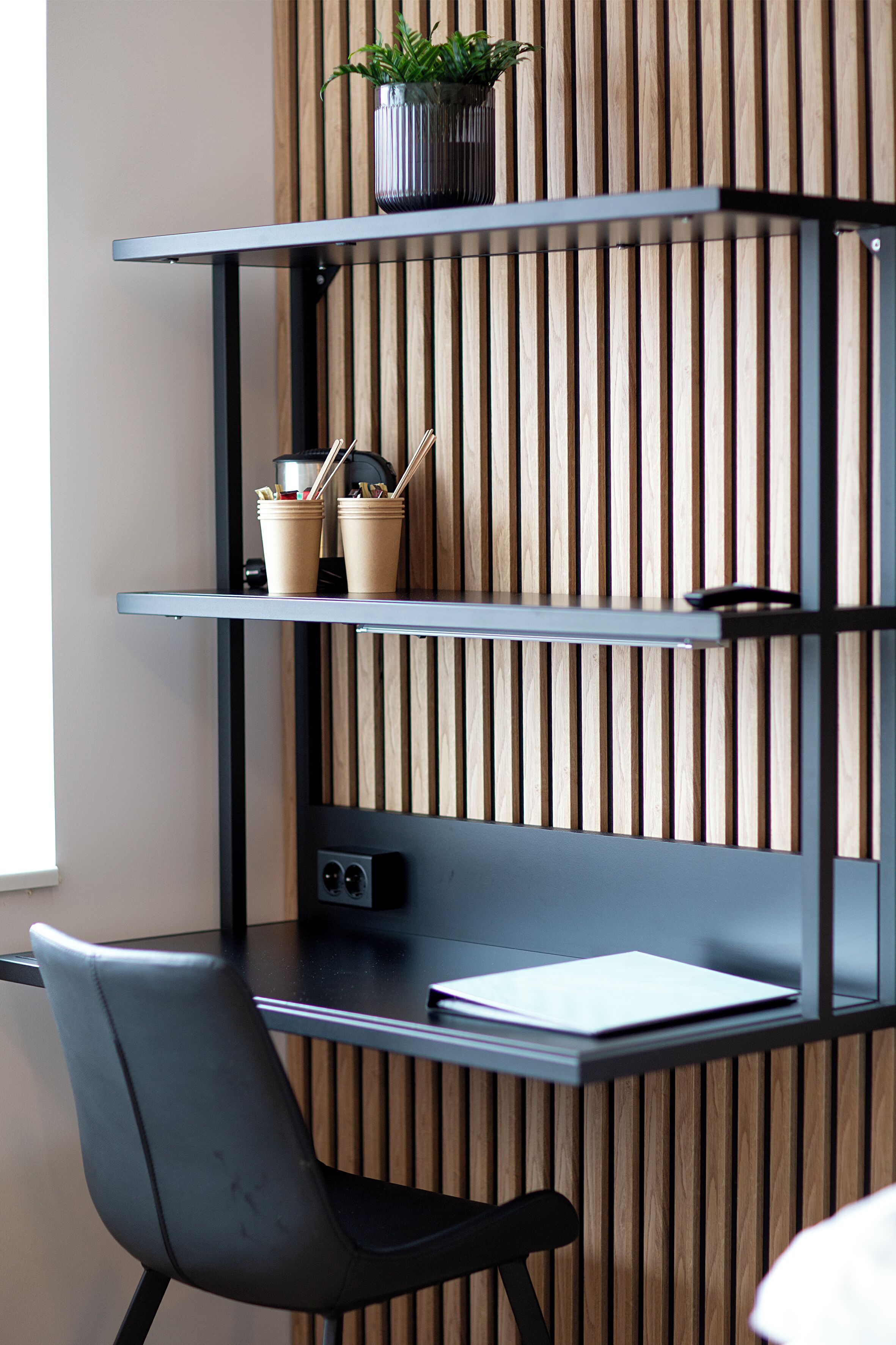 A modern workspace with a desk, chair, and shelves against a wooden slat wall.