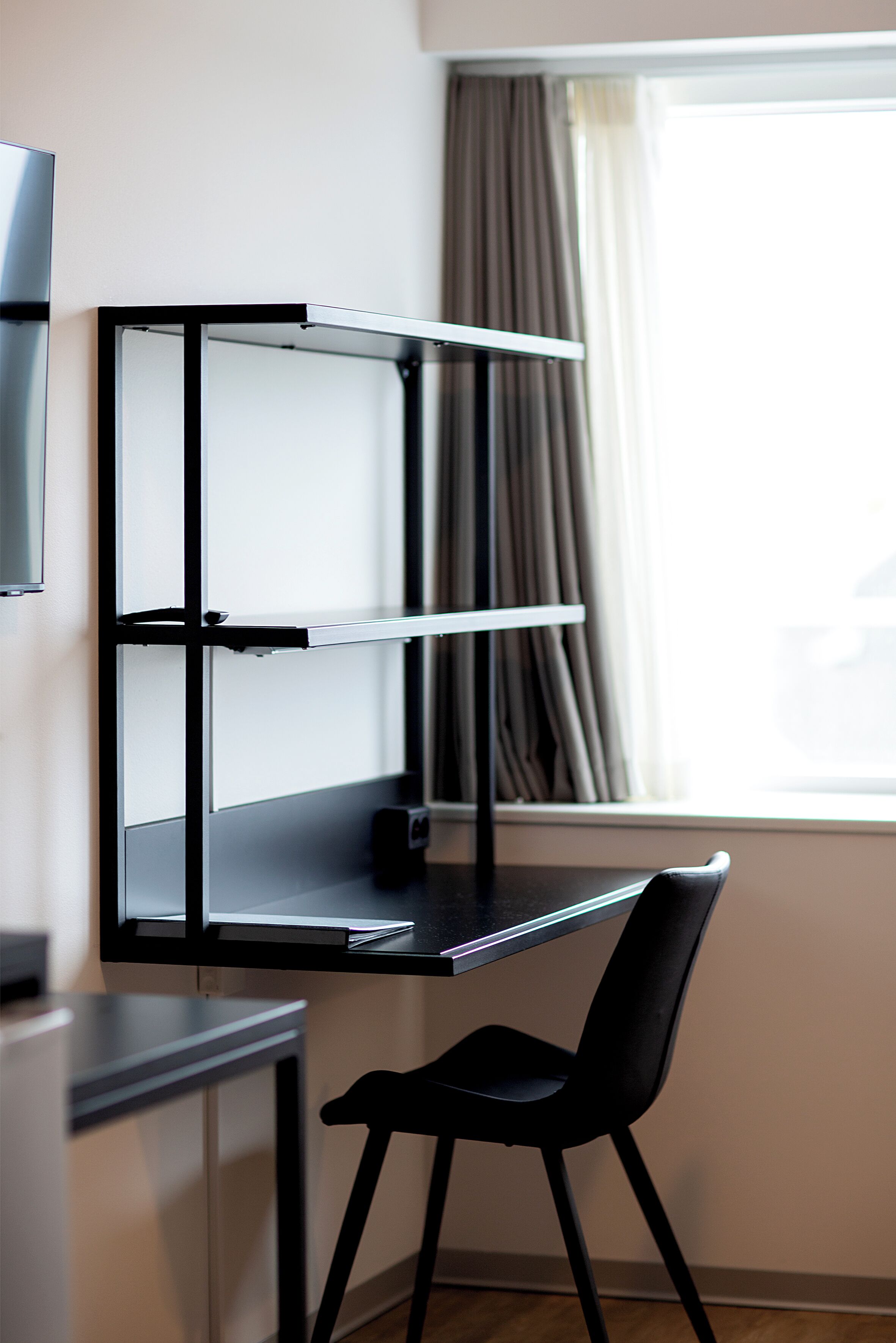 Un espacio de trabajo moderno con un escritorio negro, una silla y un televisor montado en la pared.