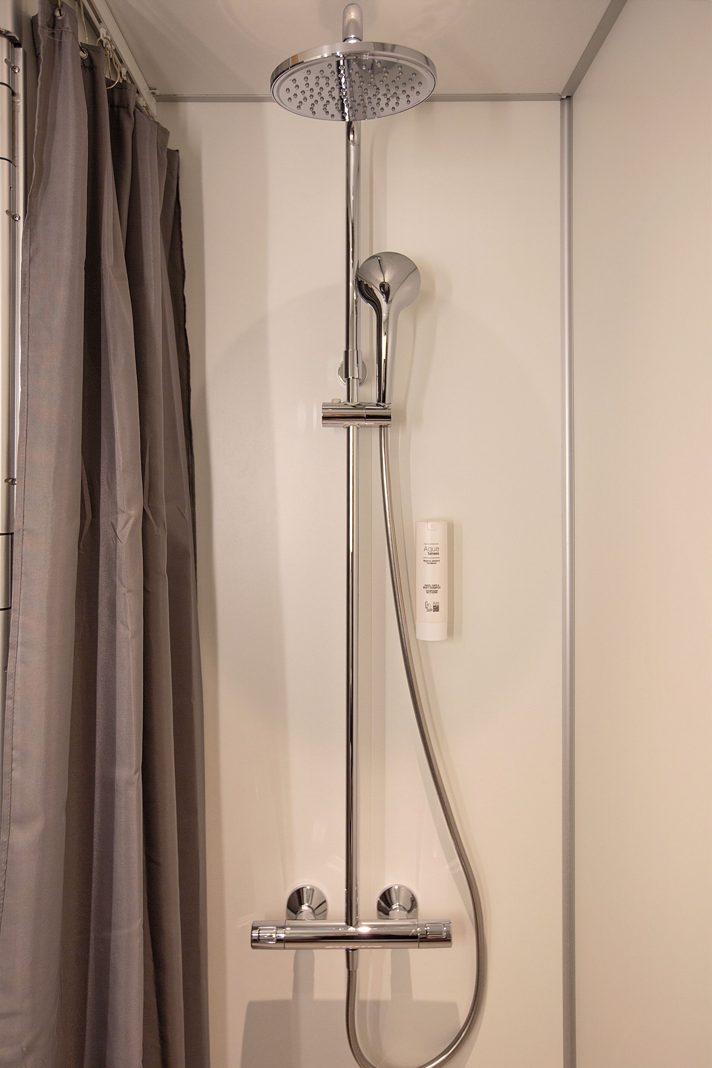 Ducha con cabezal de ducha de mano y panel de control en la pared.