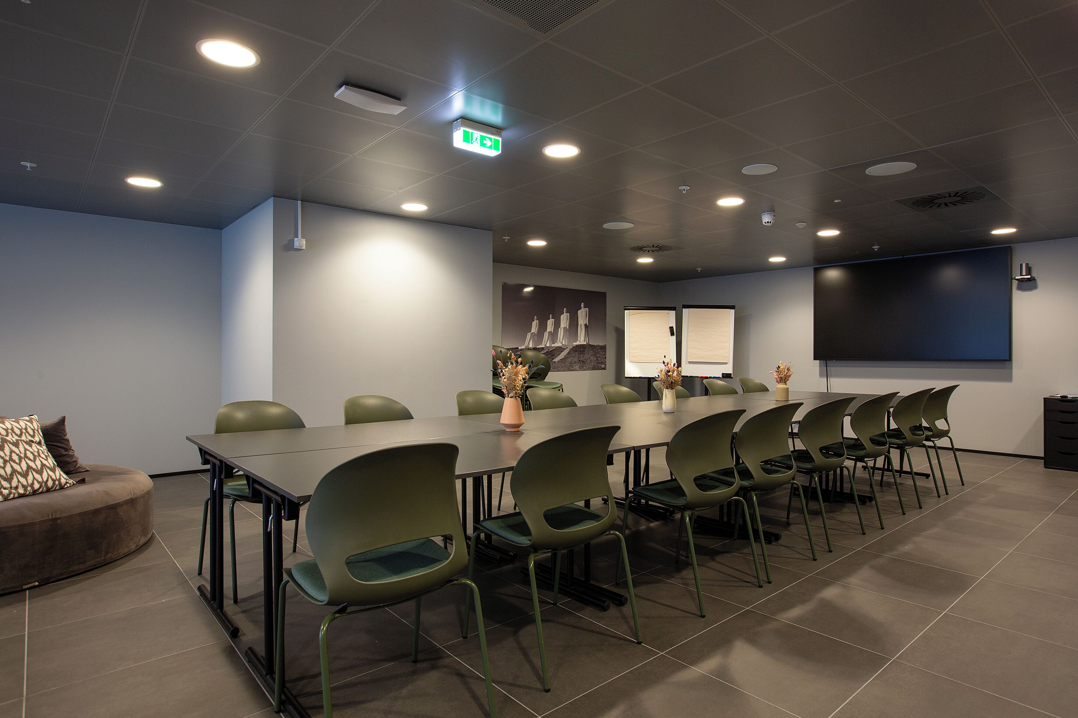 A conference room with a long table, green chairs, a brown sofa, and a projector screen.
