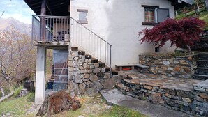 A rustic mountain house with a stone staircase, a balcony, and a view of the surrounding landscape.