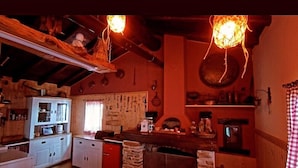 A rustic kitchen with wooden beams, a stone fireplace, and a hanging light fixture.