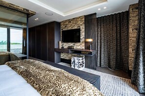 A modern bedroom with a large bed, a mounted TV, and a stone accent wall. - Aurum 101 (Cape Town)
