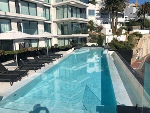 Ein modernes Hotel mit einem langen Schwimmbecken, Liegestühlen und Palmen.
