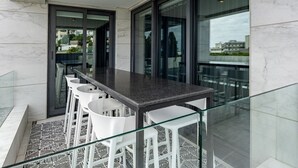 A modern balcony with a glass-top table and white bar stools, large windows, and a patterned floor. - Aurum 101 (Cape Town)