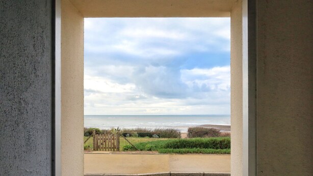 Vista desde una ventana a una playa con cielo nublado.