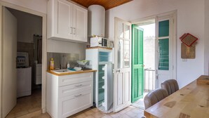 Une cuisine compacte avec des meubles blancs, un four à micro-ondes et un réfrigérateur. On y trouve une table à manger et des chaises en bois.