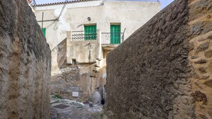 Une ruelle étroite aux murs de pierre, avec un immeuble aux volets verts et doté d’un balcon.