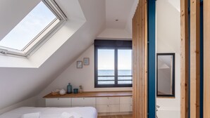 Een slaapkamer met dakraam, uitzicht op zee, een houten bankje, een bed met handdoeken en een bad.