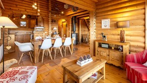Un acogedor interior de cabaña de troncos con comedor, sala de estar con sofá rojo y cocina con armarios de madera.