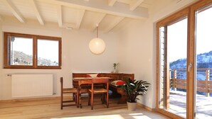 Un comedor con una mesa y sillas de madera, una lámpara colgante, una planta en maceta y vistas a un paisaje nevado a través de grandes puertas corredizas de vidrio.