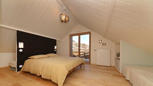 Un dormitorio con una cama grande, suelo de madera, techo inclinado y vistas a una ladera a través de una puerta corredera.