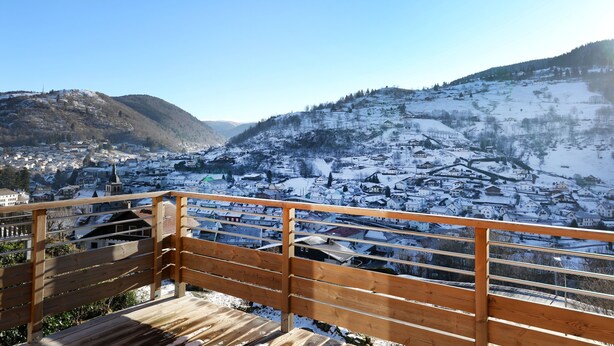 Una terraza de madera con vistas a un pueblo cubierto de nieve y montañas.