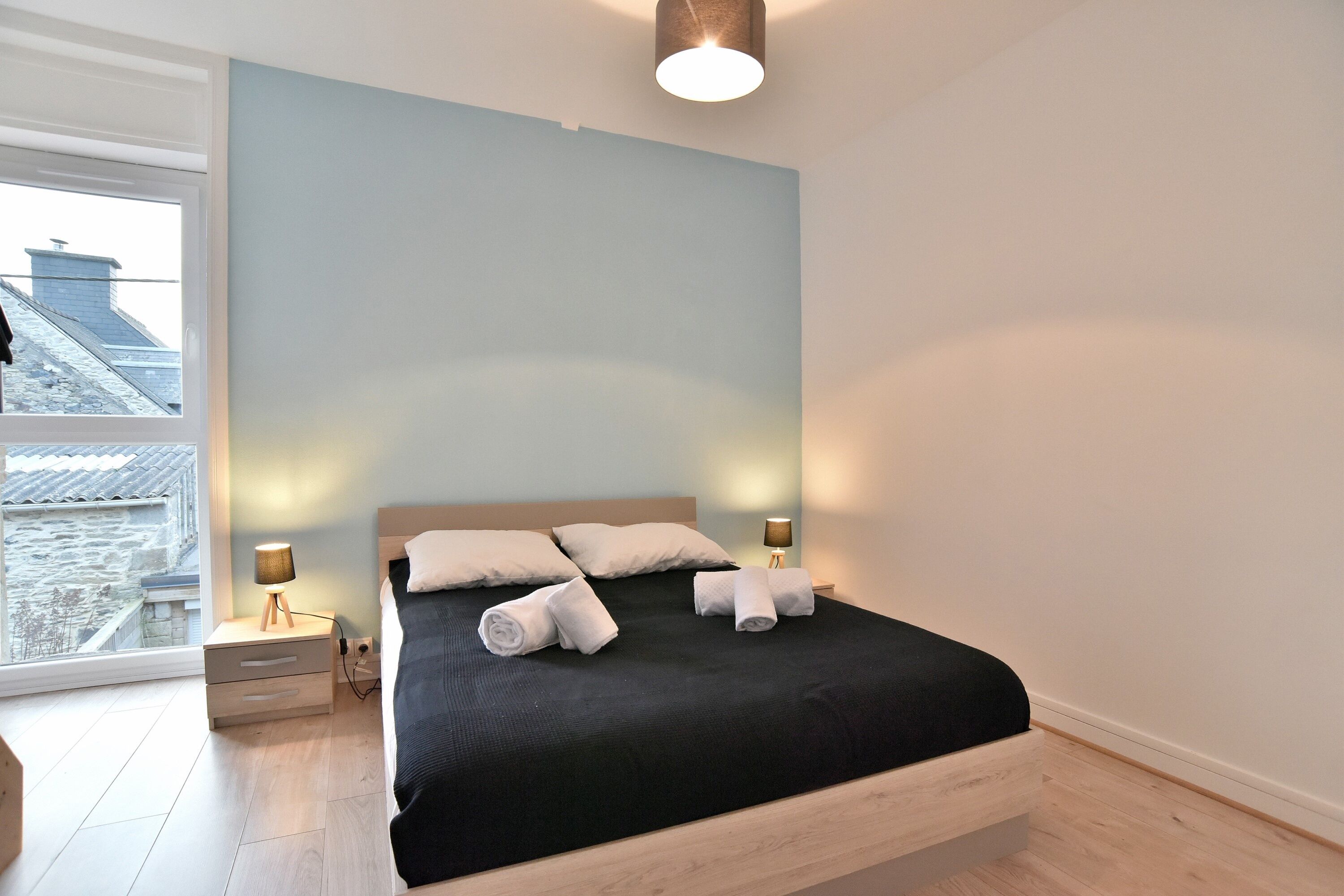 A modern bedroom with a large bed, two bedside tables, and a view of a cityscape through a large window.