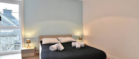 A modern bedroom with a large bed, two bedside tables, and a view of a cityscape through a large window.